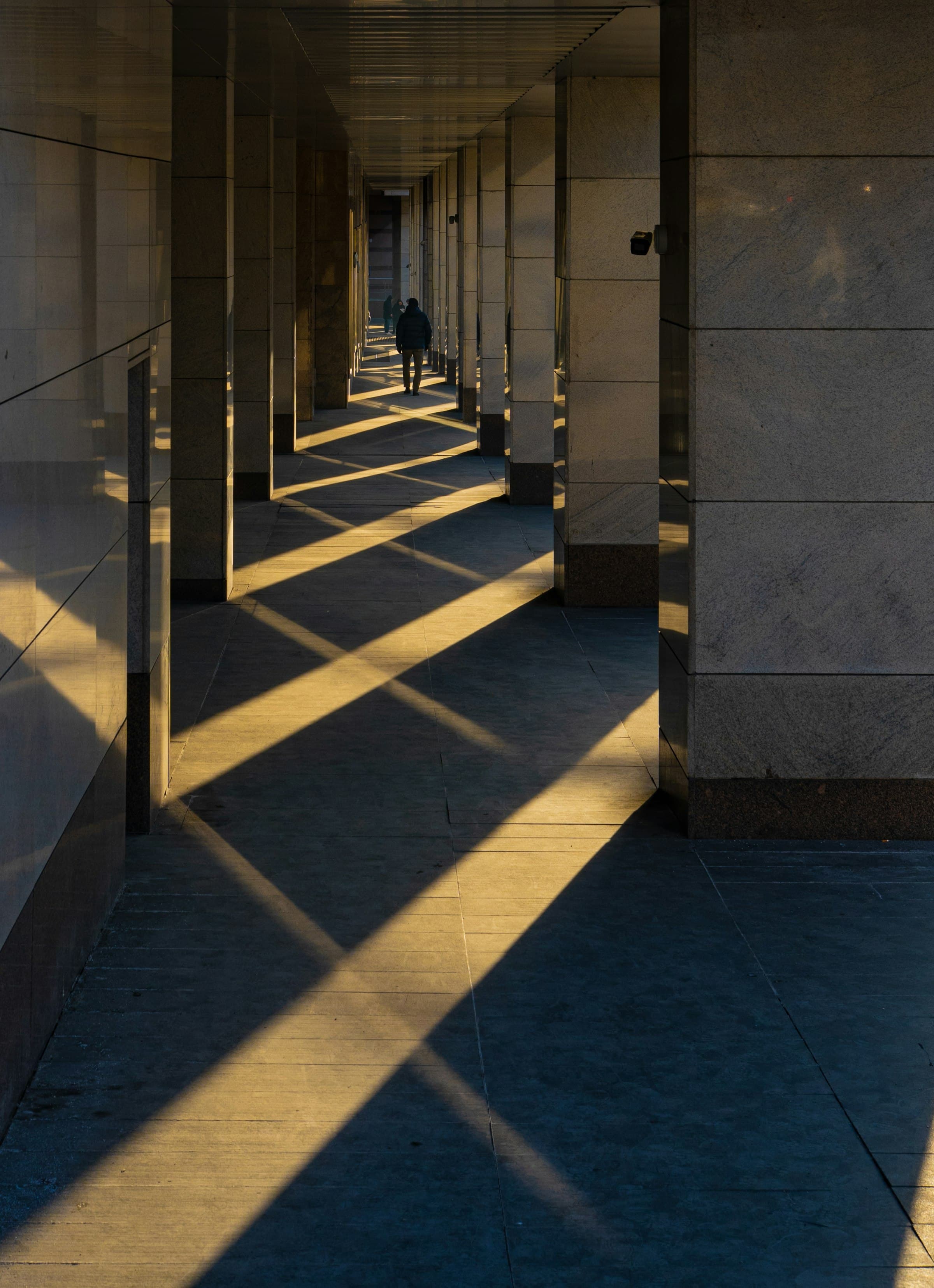 A figure walking through a colonnade striped with light